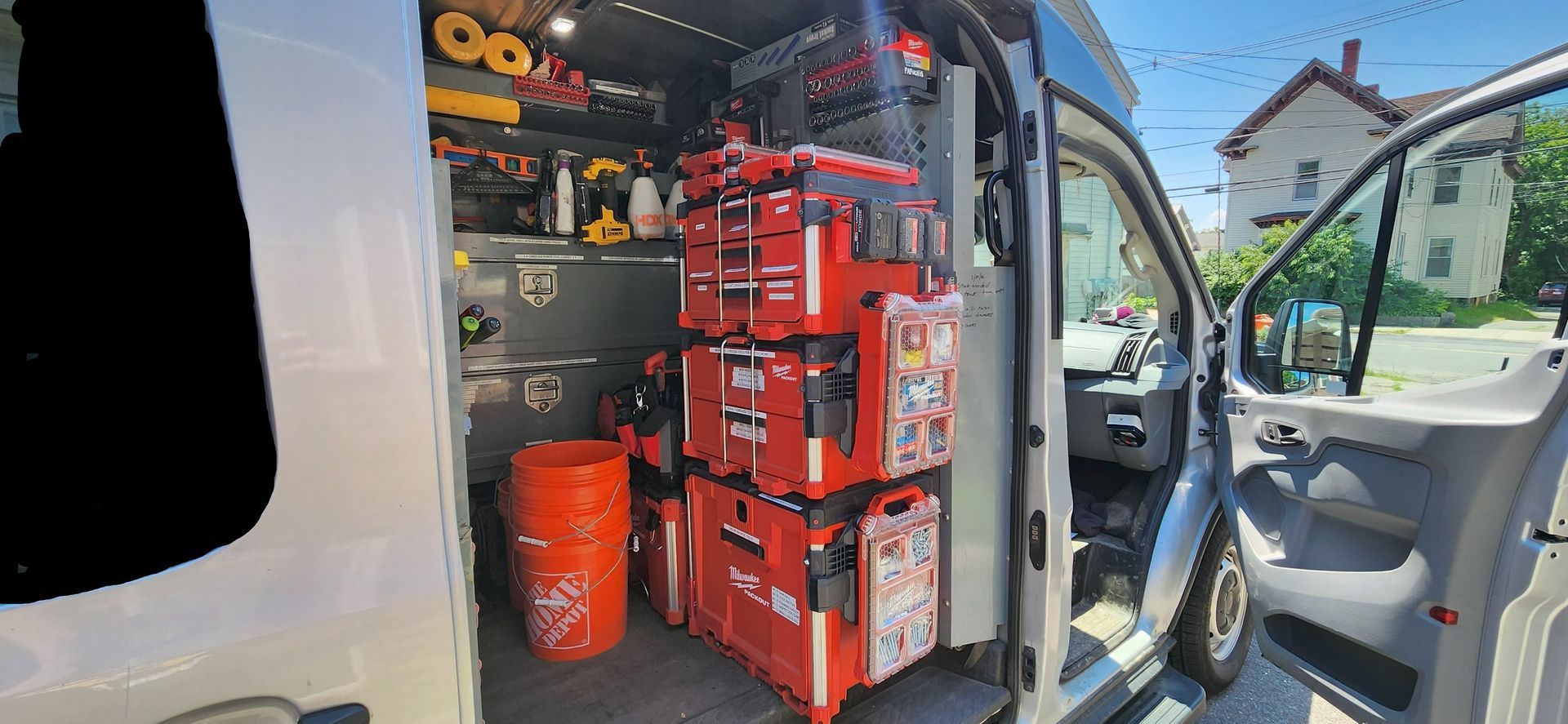 Open van cargo area packed with red tools and equipment, doors open in a sunny driveway.