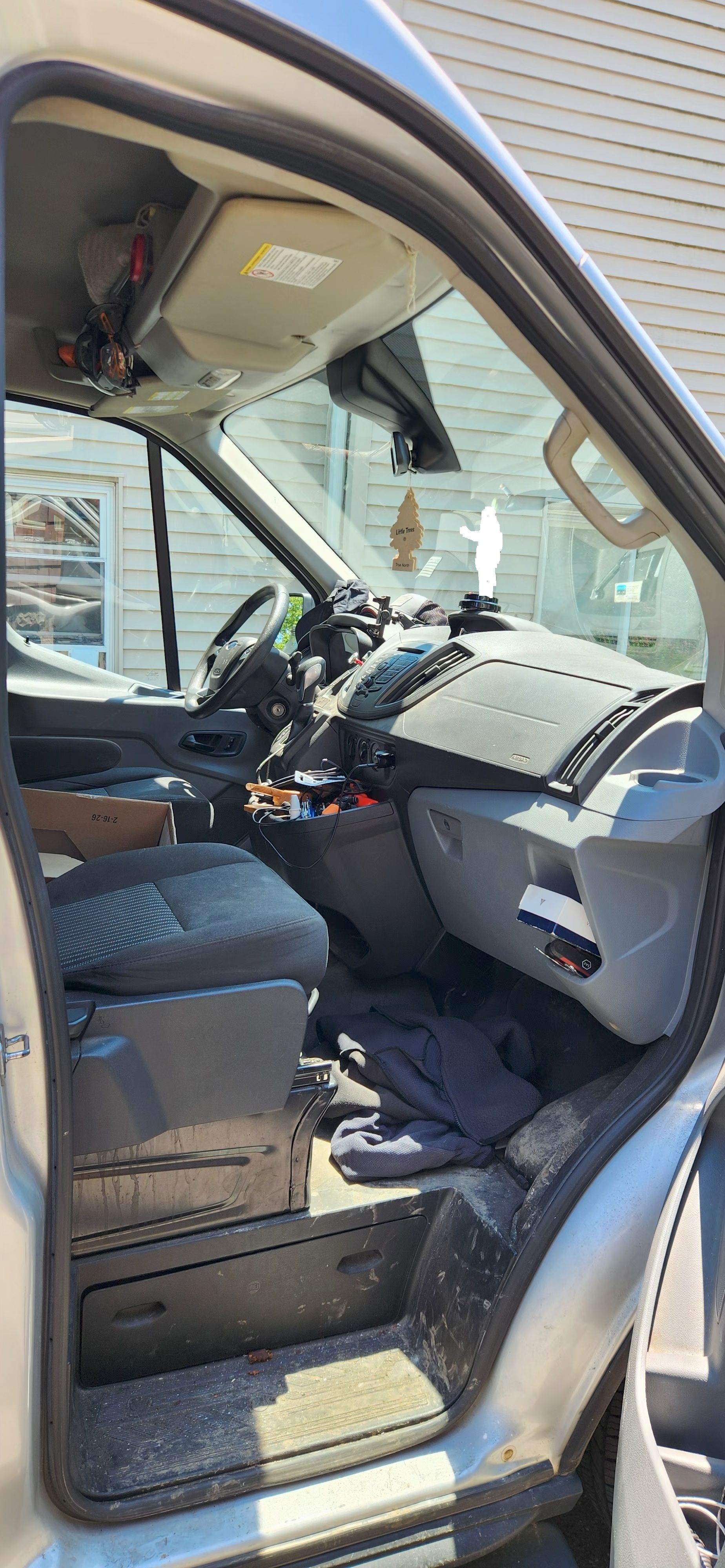 Open car door showing a cluttered front seat and dashboard inside a gray vehicle.