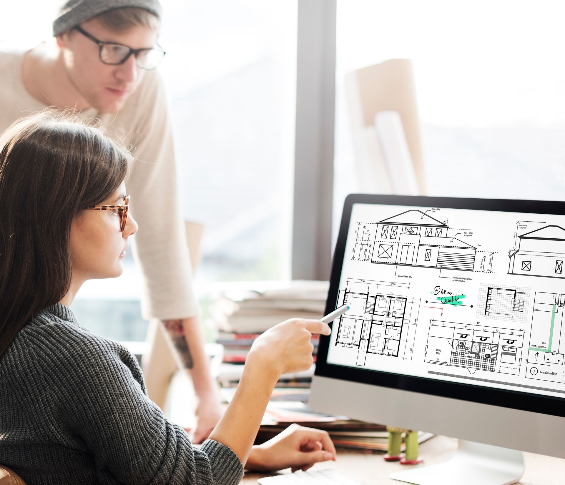Woman points at a computer screen with architectural plans; a man looks over her shoulder.
