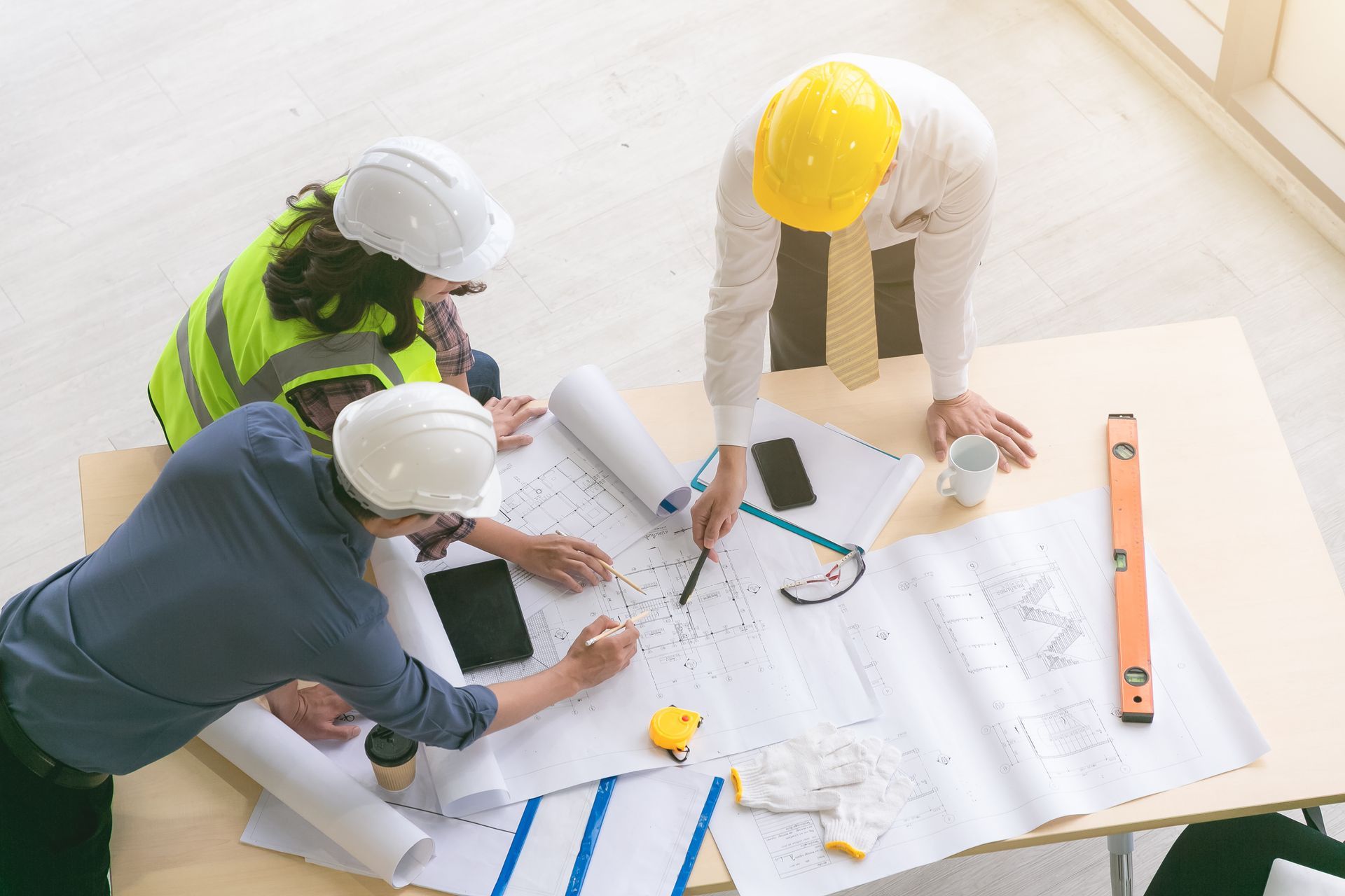 Construction team reviewing blueprints at a desk, wearing hard hats and safety vests.