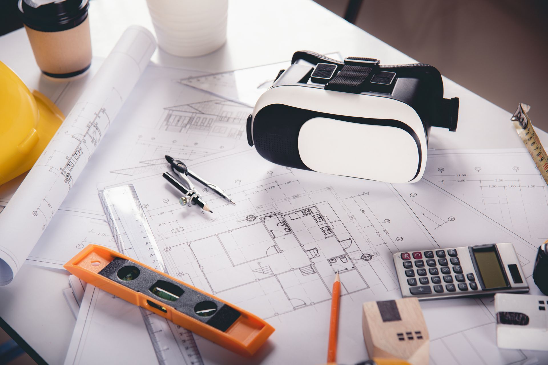 Person reviewing house plans with a model house, blueprints, and a calculator on a wooden table.