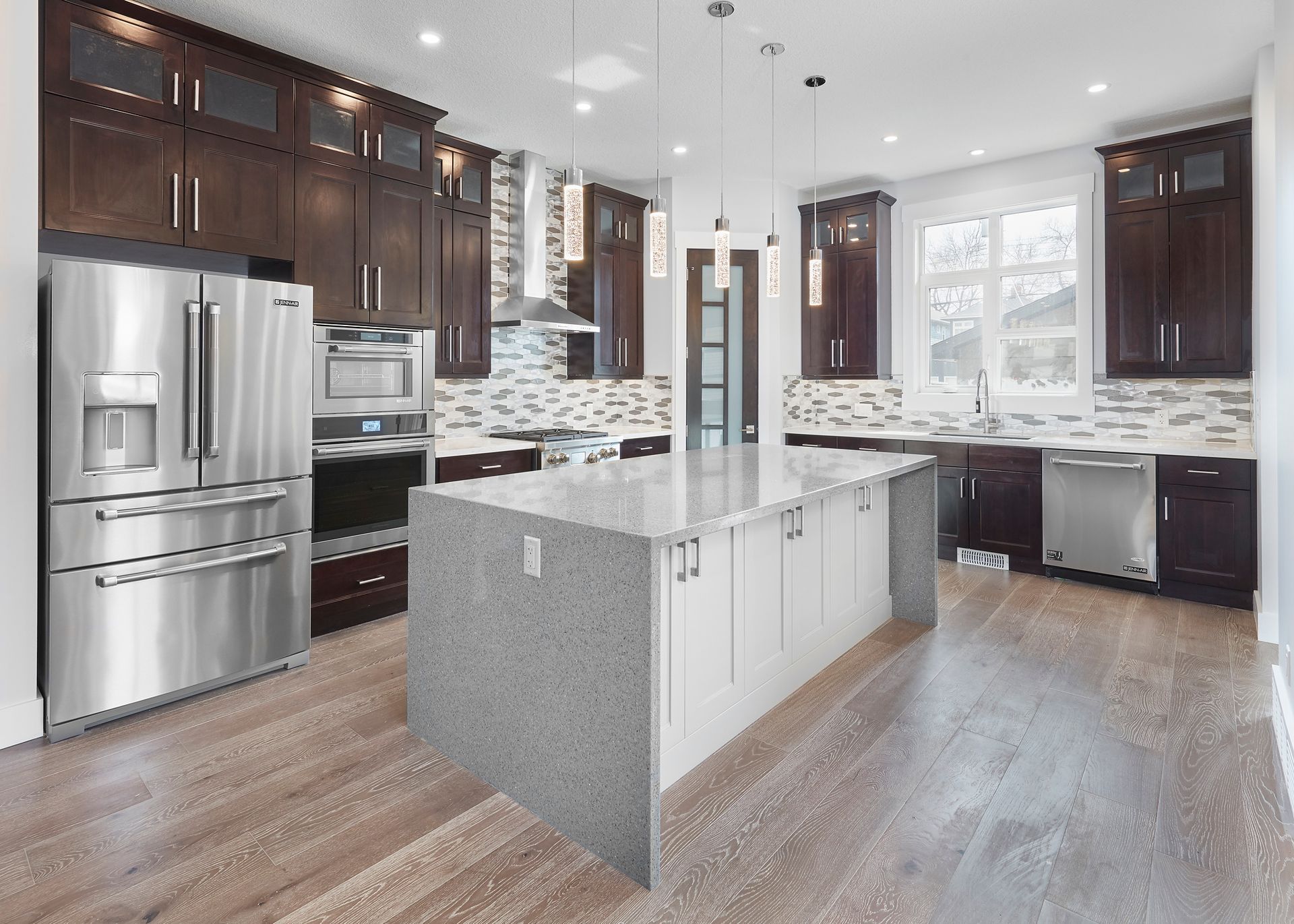 Modern kitchen with dark brown cabinets, stainless steel appliances, and a large island with a gray countertop.