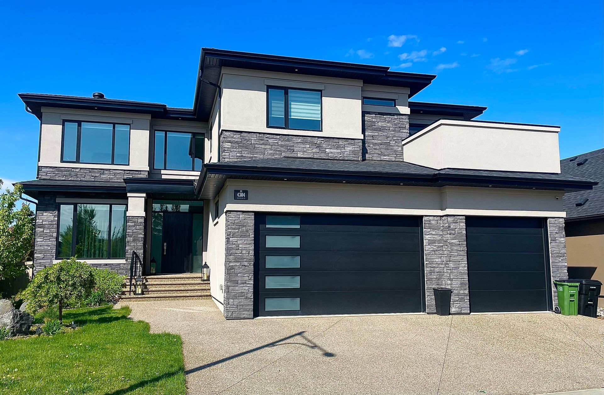Two-story house with gray stone and black garage doors on a sunny day.