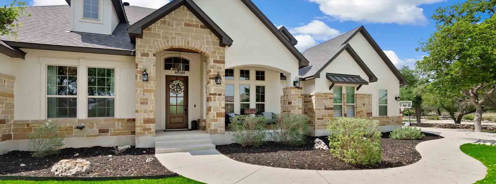 Exterior view of a house with a stone arch entryway, white walls, and a paved walkway leading to a front door.