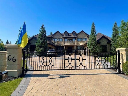 Large house behind black decorative gate; Ukrainian flag flies.