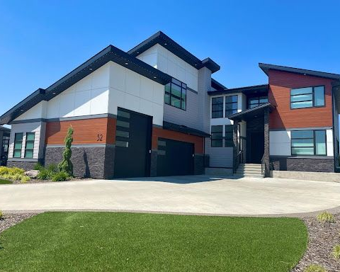 Modern two-story house with gray and white exterior, red accents, and a large driveway under clear blue sky