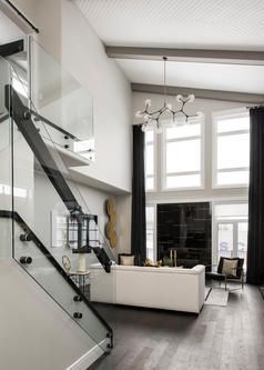 Modern living room with a staircase and a black fireplace, high ceilings, and a large chandelier.