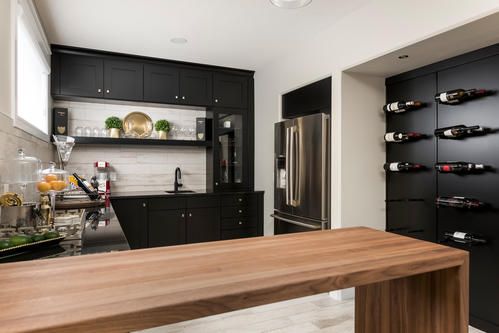 Modern black kitchen with wood countertop, stainless steel refrigerator, and wine rack.