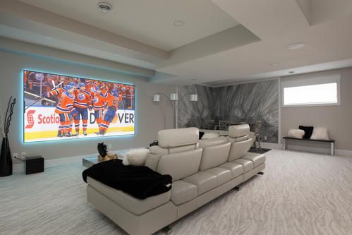 Modern living room with large screen displaying hockey game, light-colored sectional sofa, patterned carpet, and decorative wall art.