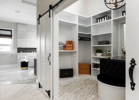 White walk-in closet with sliding barn door, next to a light gray bathroom.