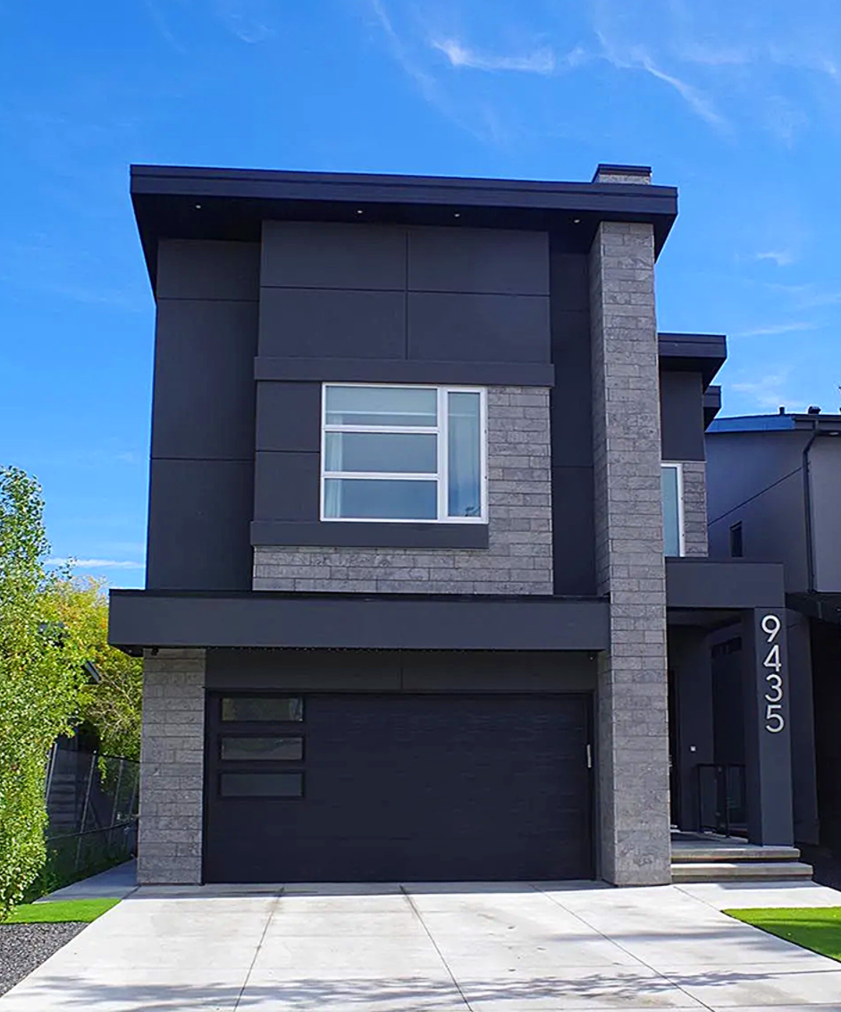 Modern two-story house with dark gray siding and stone accents; driveway and lawn.