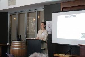 A woman is standing at a podium giving a presentation in front of a projector screen.