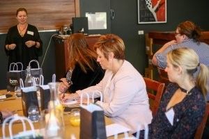 A group of women are sitting at a table with a woman standing behind them.