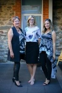 Three women are standing next to each other in front of a brick building.
