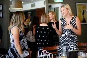 A group of women are standing around a table talking to each other.