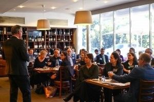 A man is standing in front of a group of people sitting at tables in a restaurant.