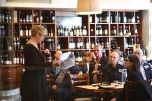 A woman is standing in front of a group of people in a restaurant.