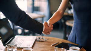 A man and a woman are shaking hands over a table.
