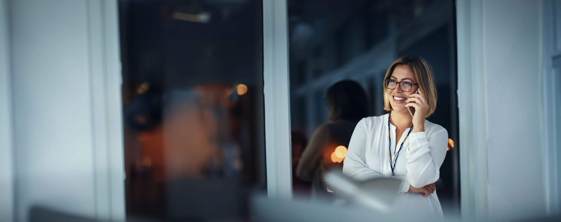 A woman is sitting in front of a window talking on a cell phone.