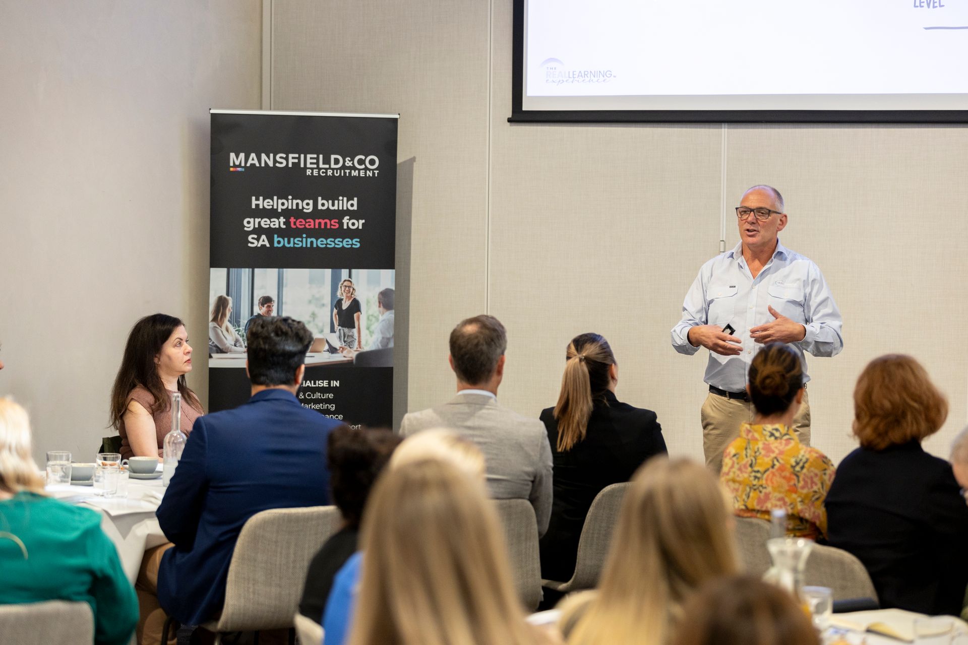 A man is giving a presentation to a group of people sitting at tables.