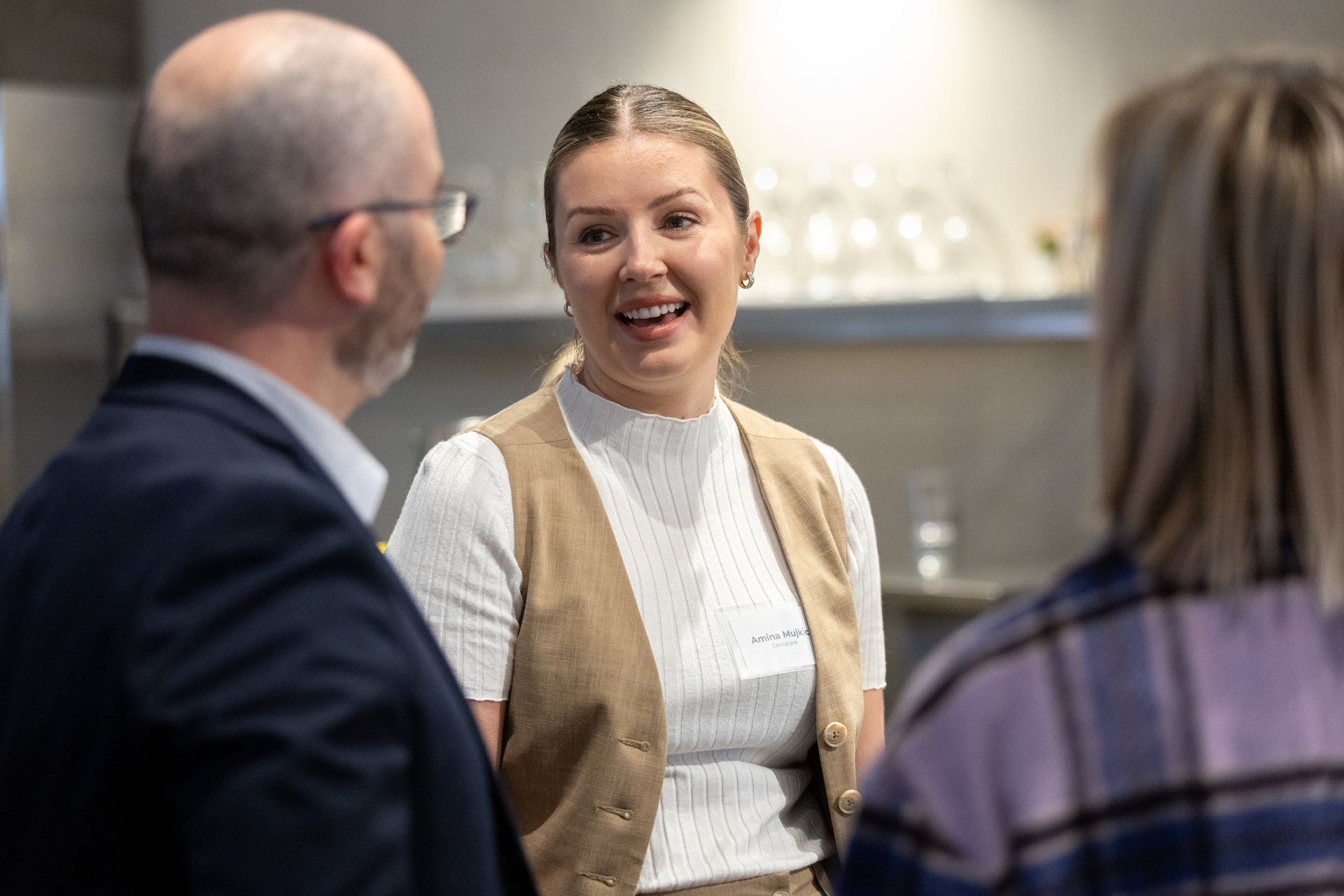 A group of people are standing around talking to each other in a kitchen.
