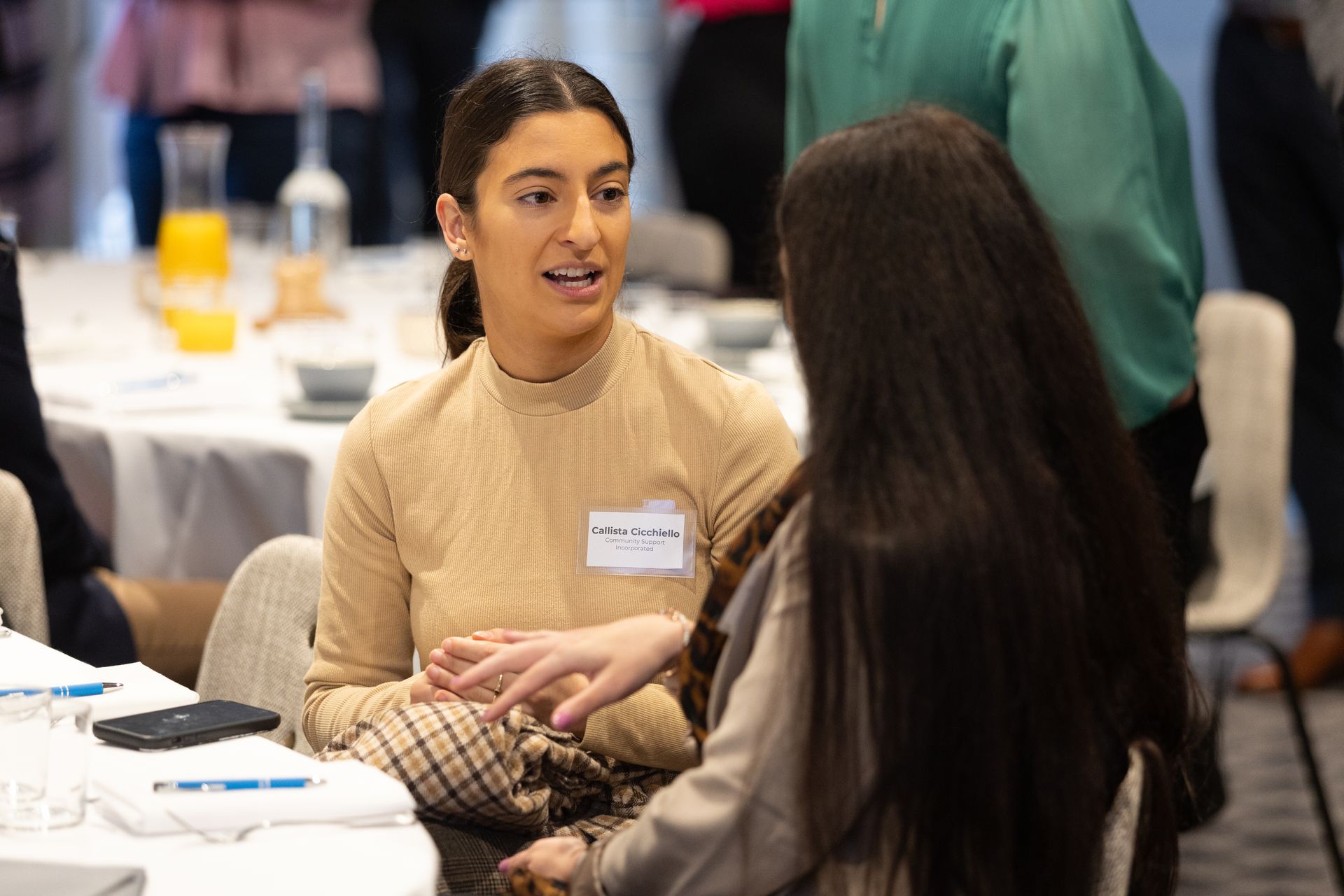 Two women are sitting at a table talking to each other.