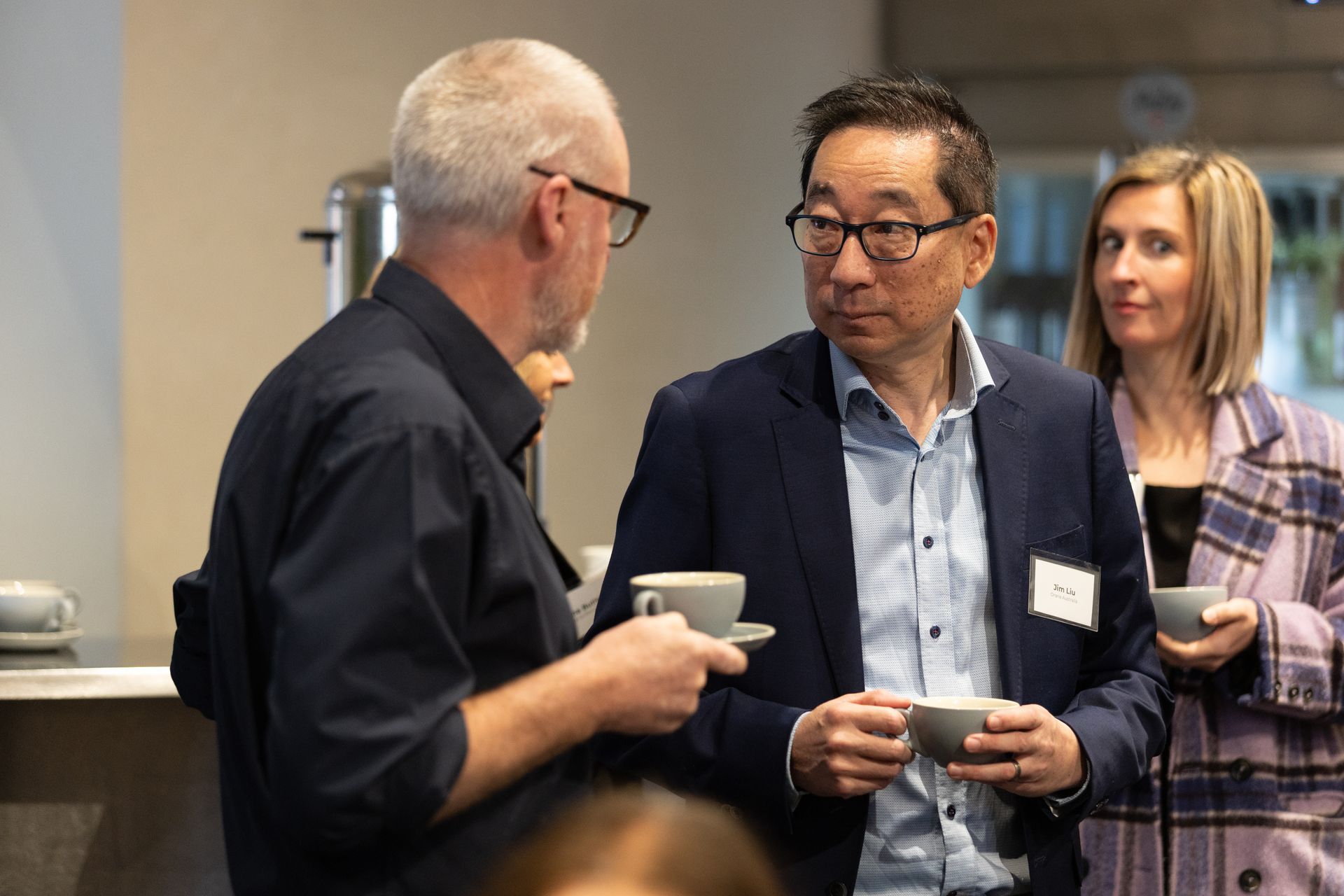 A group of people are standing around talking and drinking coffee.