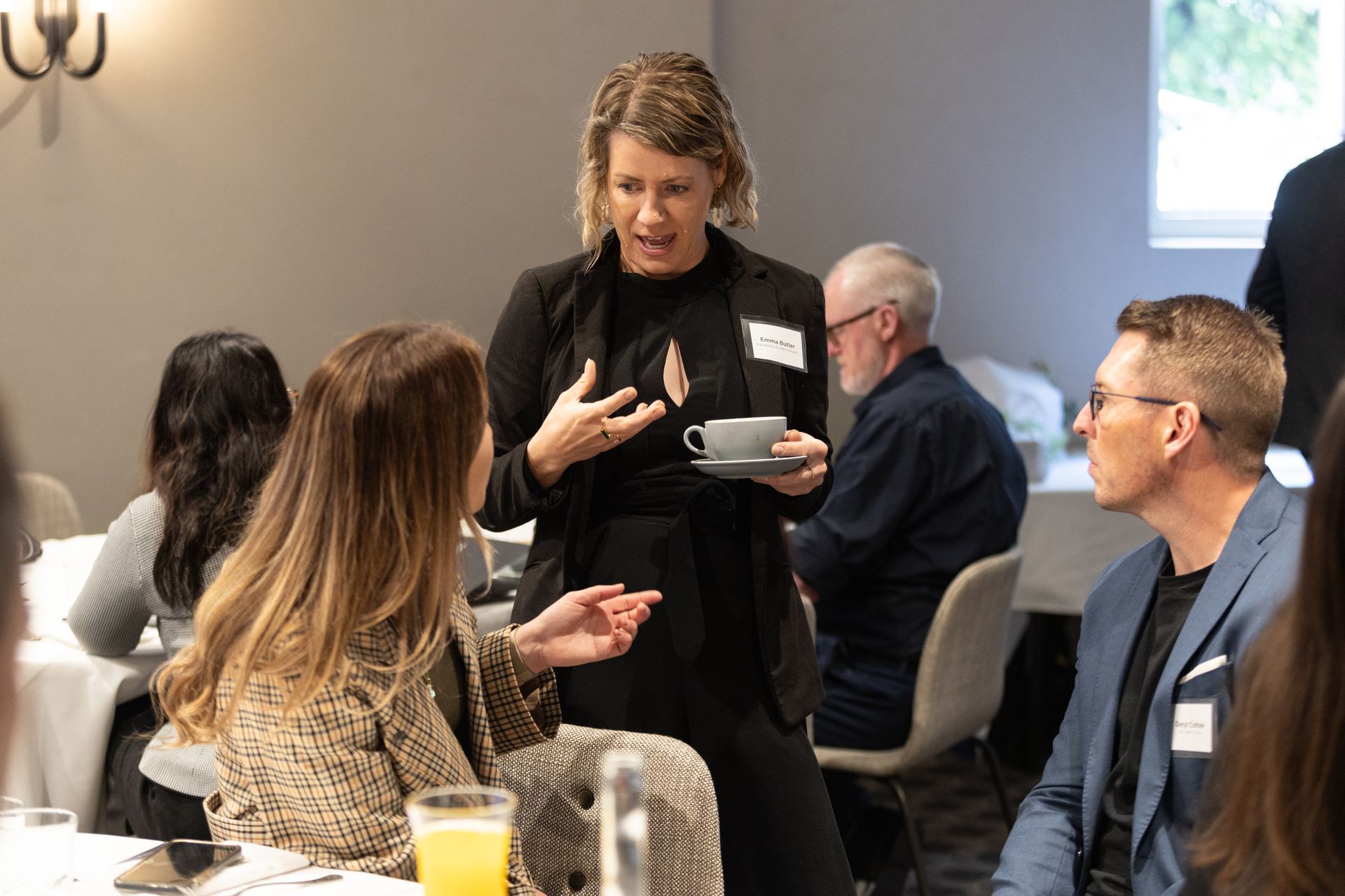 A woman is talking to a group of people while holding a cup of coffee.