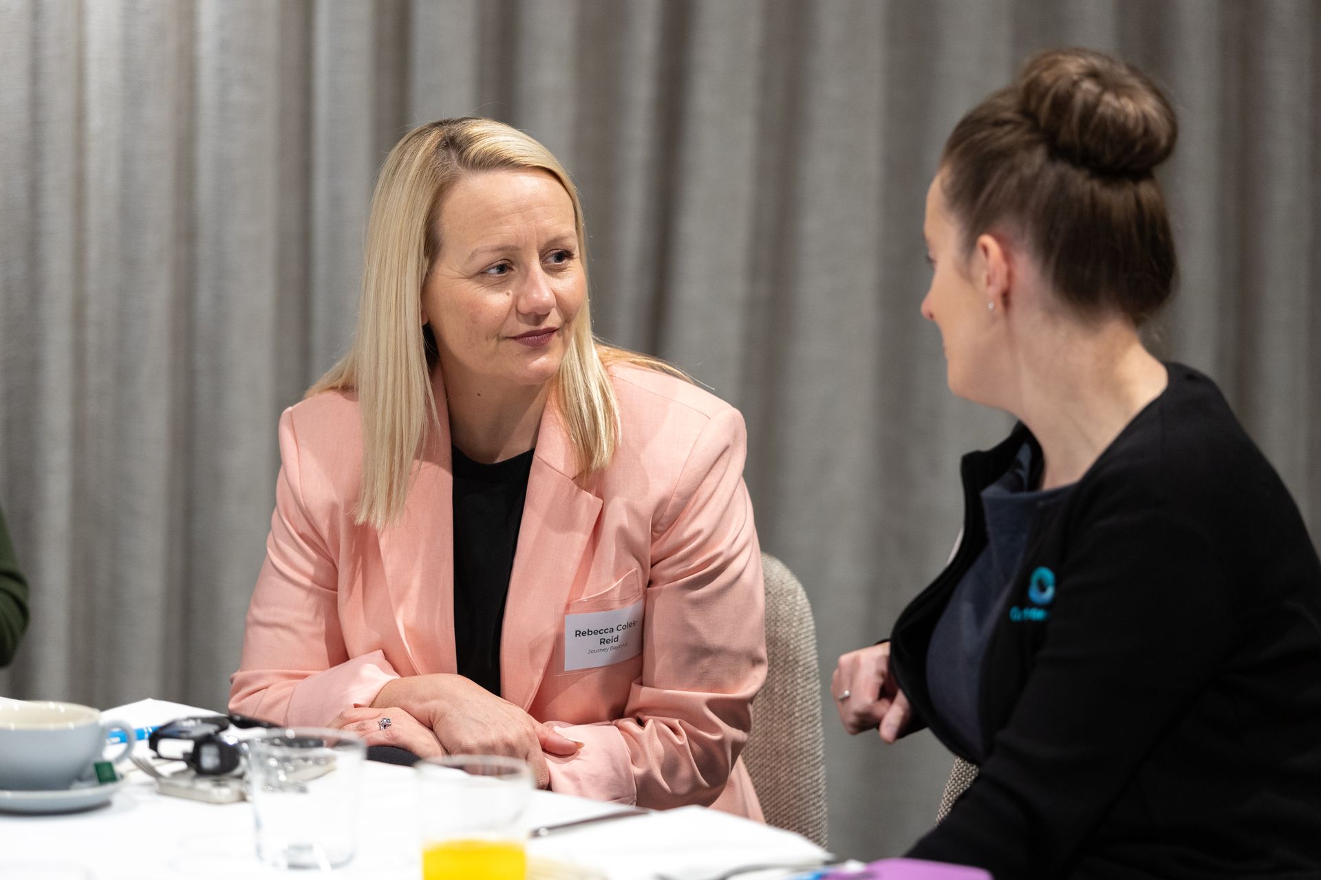 Two women are sitting at a table talking to each other.