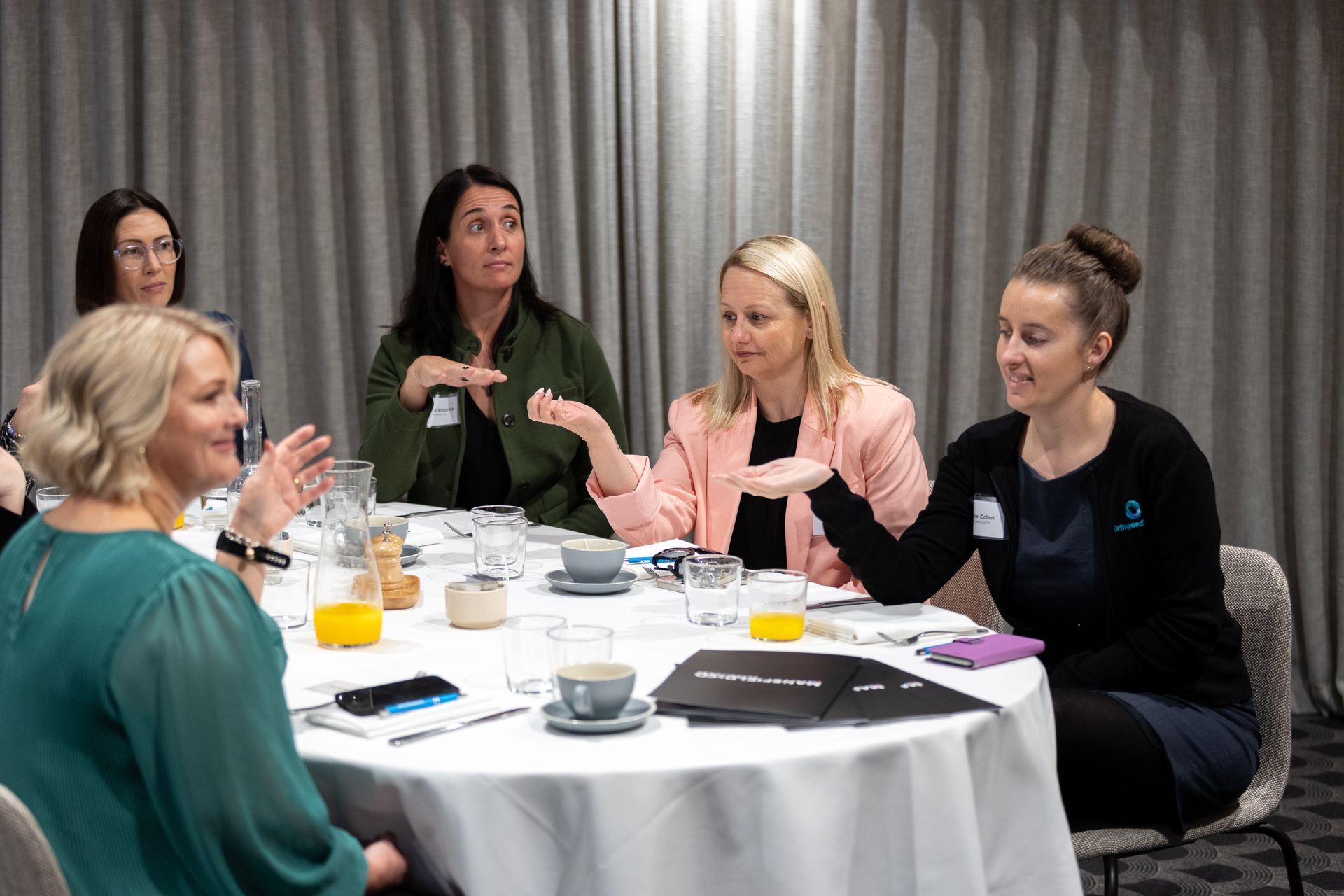 A group of women are sitting at a table talking to each other.