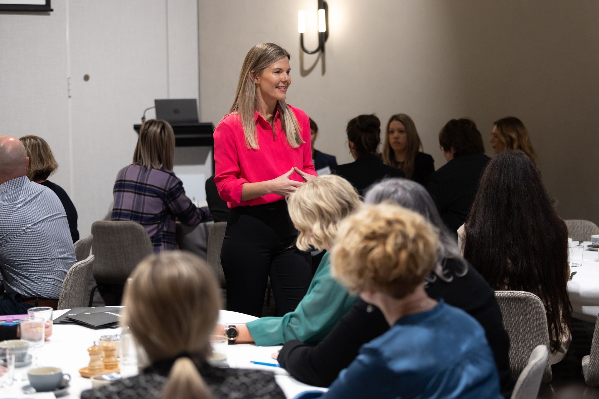 A woman is standing in front of a group of people sitting at tables.