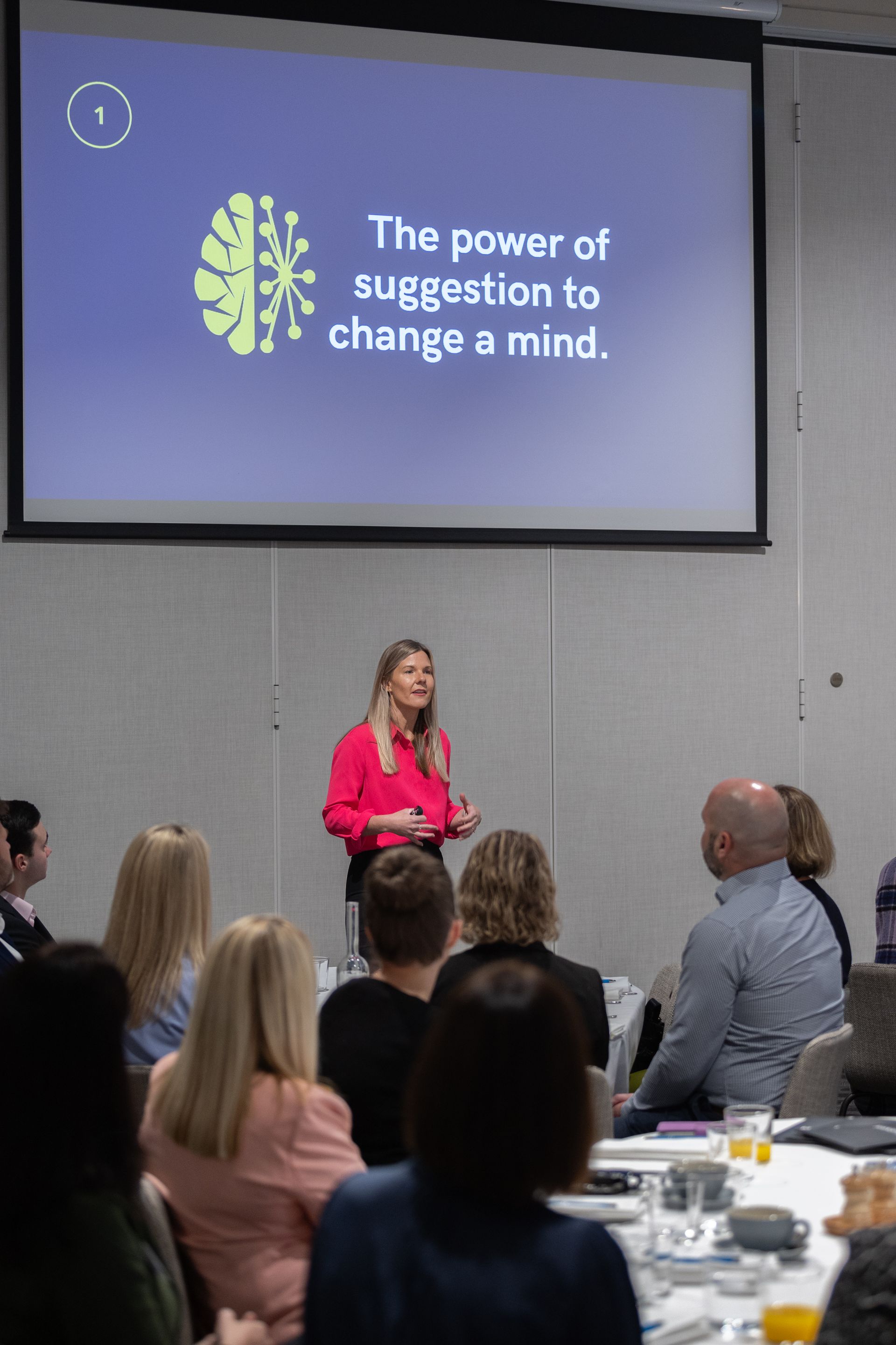 A woman is giving a presentation to a group of people in front of a large screen.
