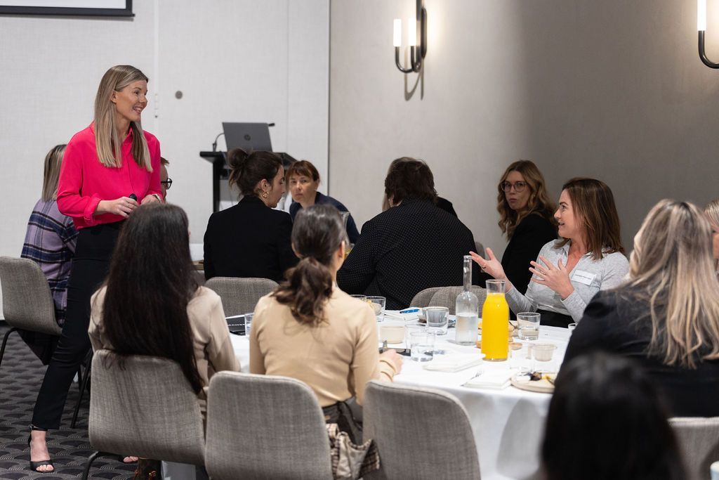 A woman is giving a presentation to a group of people sitting at tables.