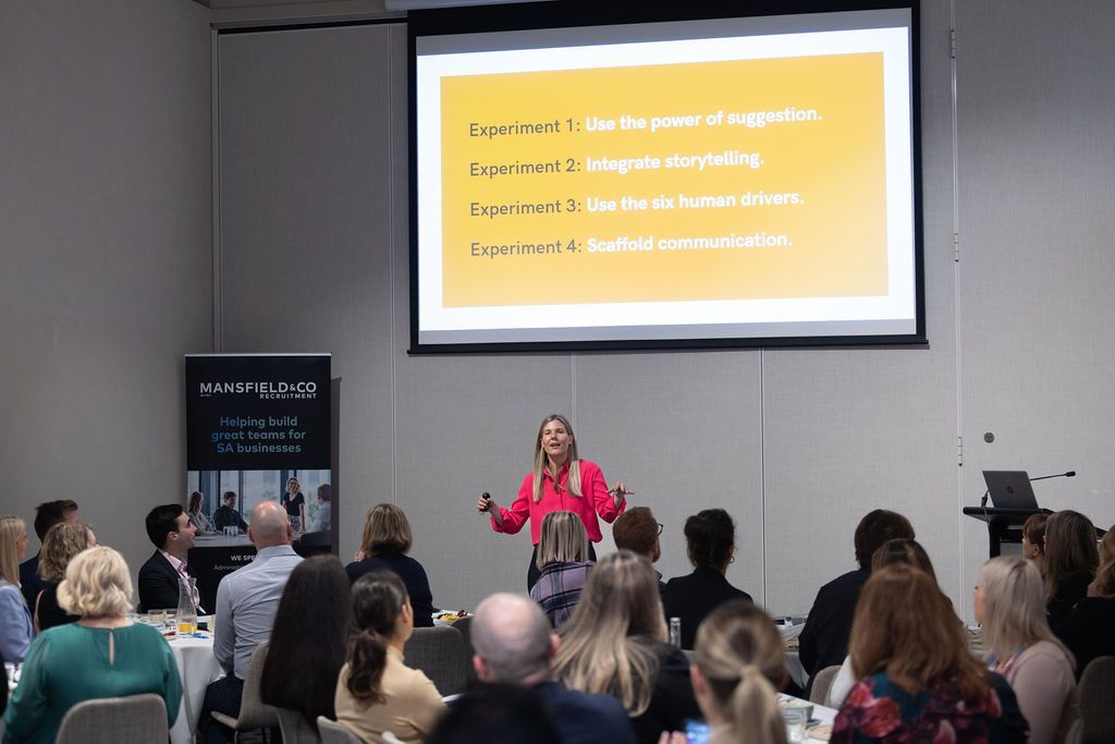 A woman is giving a presentation to a group of people in front of a large screen.