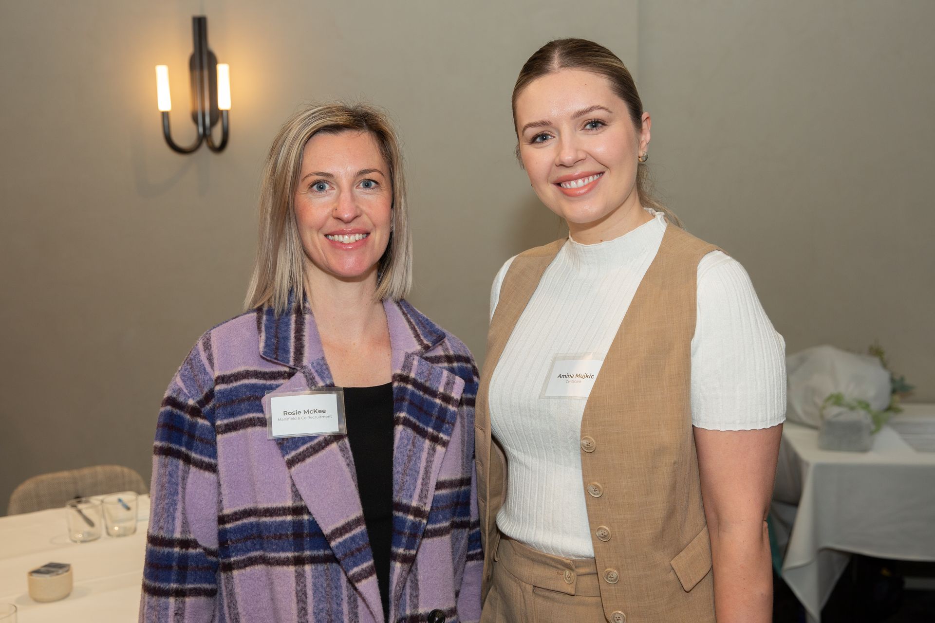 Two women are standing next to each other in a room and smiling.