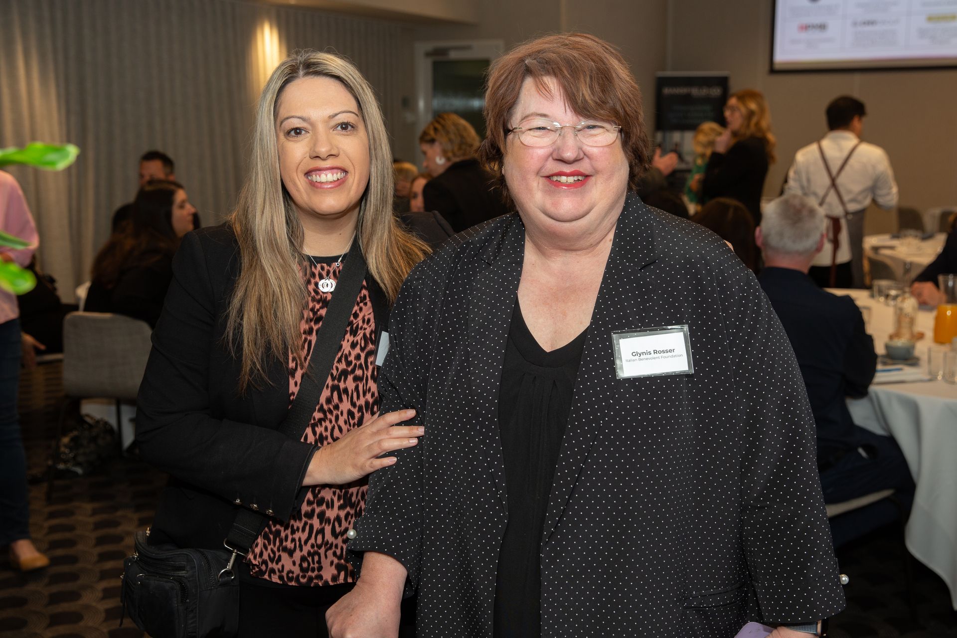 Two women are posing for a picture together at a conference.