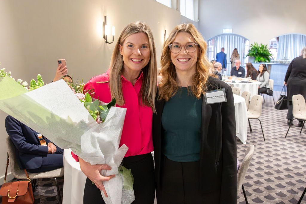 Two women are standing next to each other in a room holding a bouquet of flowers.