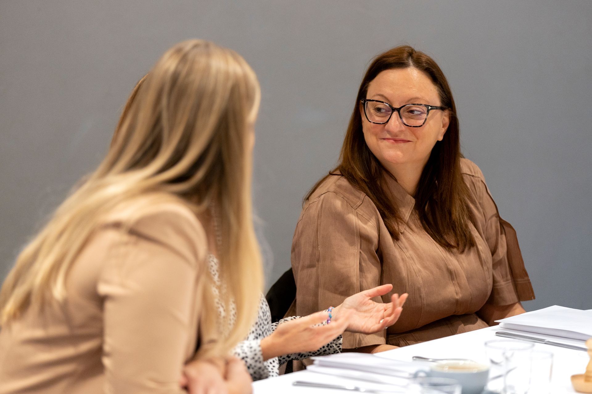 Two women are sitting at a table talking to each other.