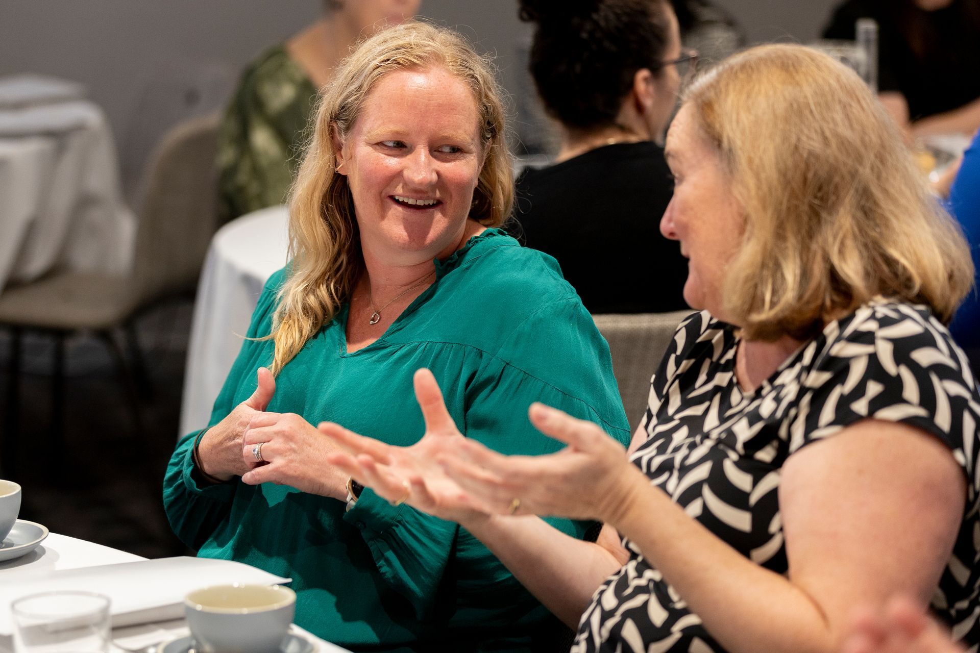 Two women are sitting at a table talking to each other.