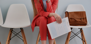 A woman in a red suit is sitting in a chair holding a piece of paper.