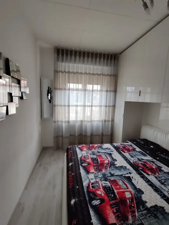 Una camera da letto con un letto con una trapunta a tema autobus rosso londinese, tende trasparenti, pavimento chiaro e opere d'arte appese alle pareti.
