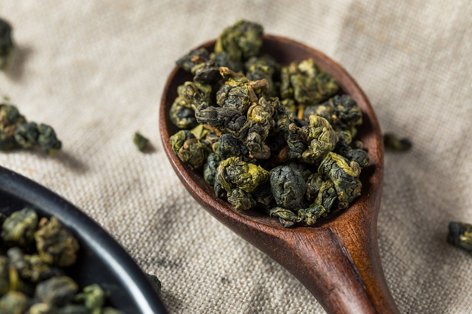 A wooden spoon filled with green tea leaves on a table.