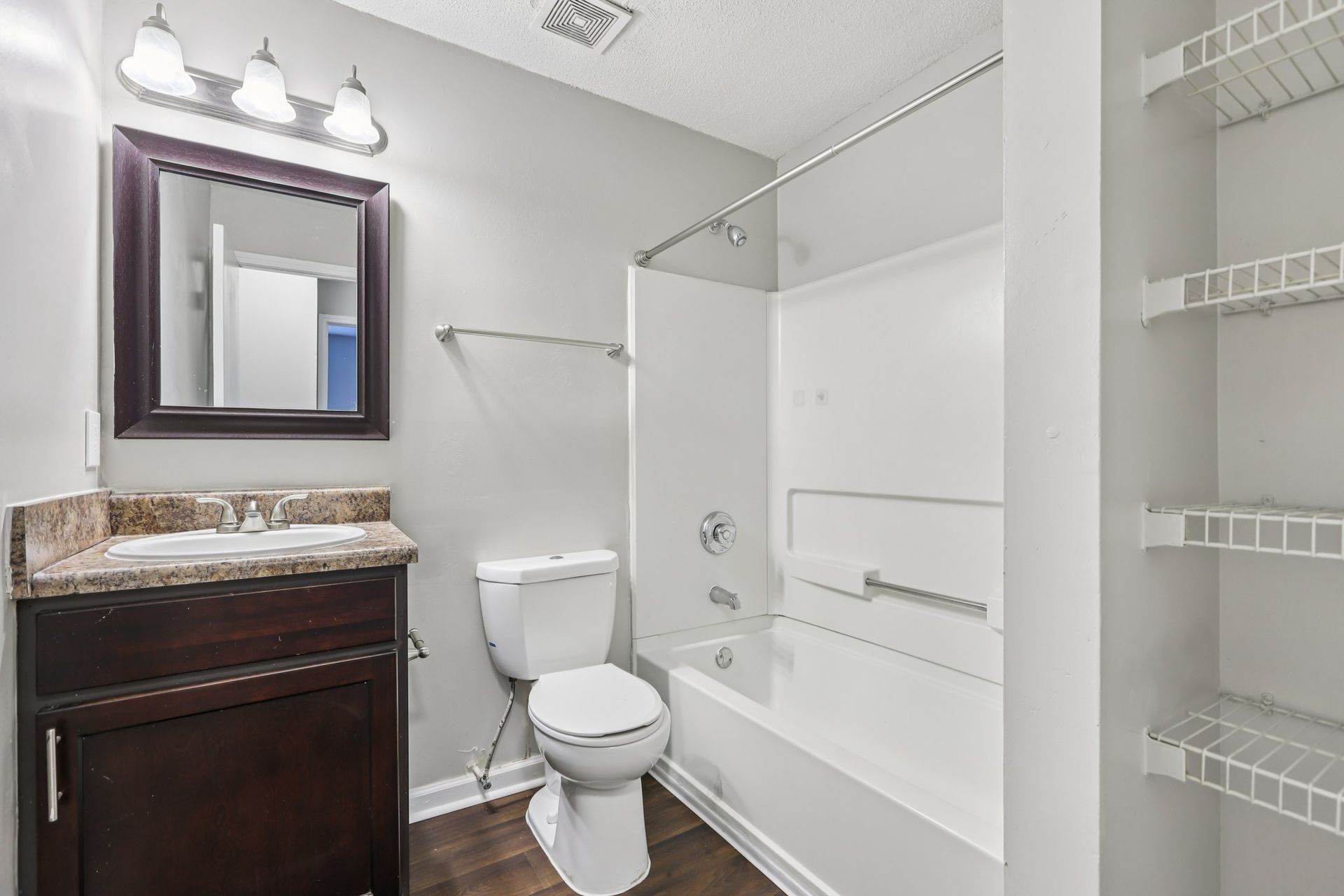 A bathroom with a dark wood vanity, a white toilet, a bathtub with a shower head, and built-in wire shelving.