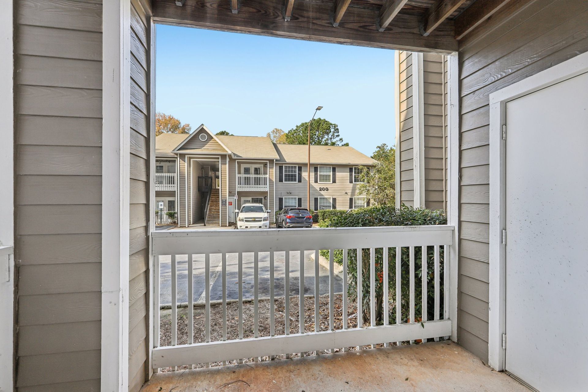A view from a covered balcony looking out at another apartment building across a parking lot with parked cars.