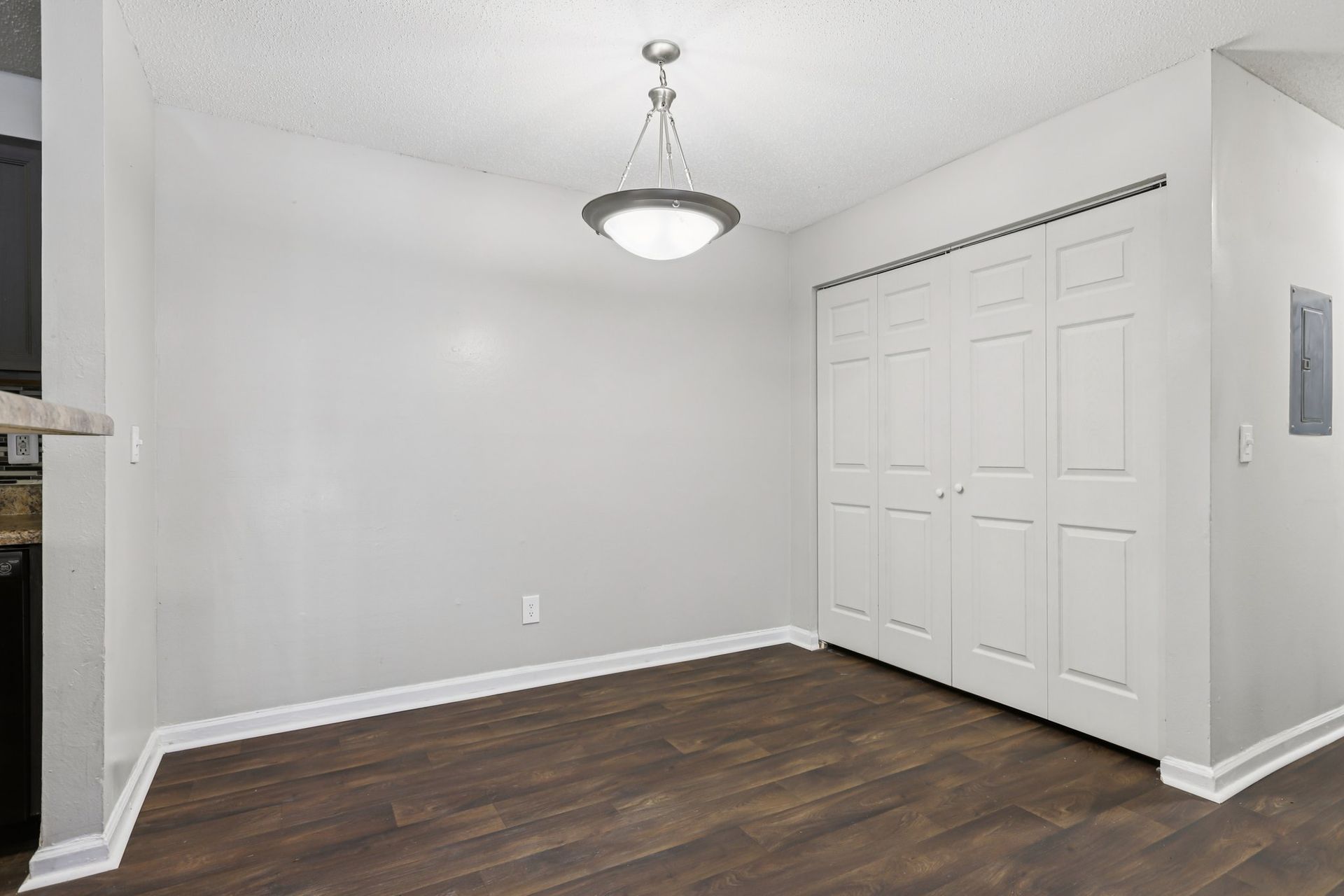 Empty dining area with white walls, dark wood-look flooring, a modern pendant light, and white folding closet doors.