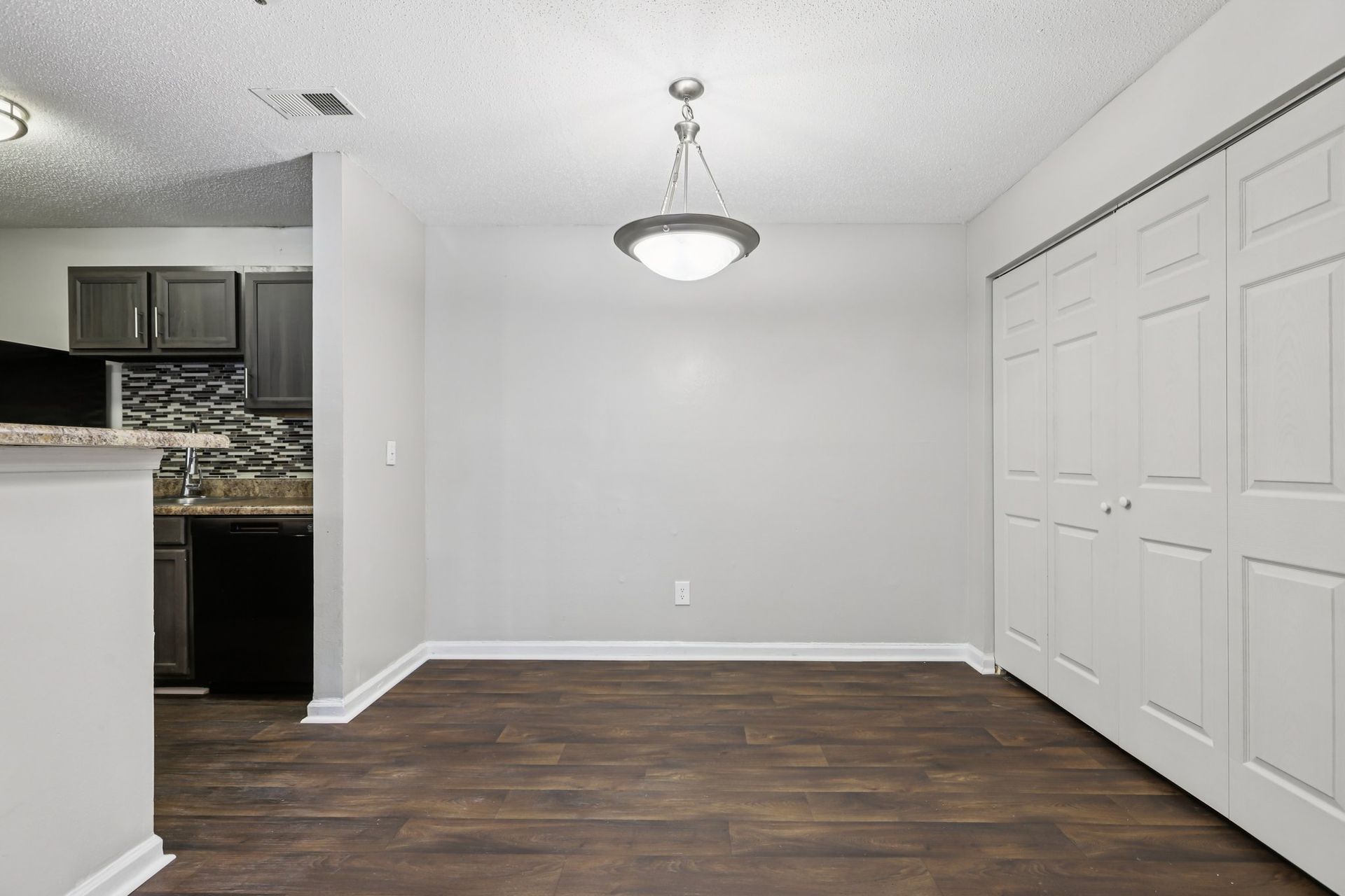 A dining area with wood-look floors, a white wall, a hanging light fixture, and white bi-fold closet doors.