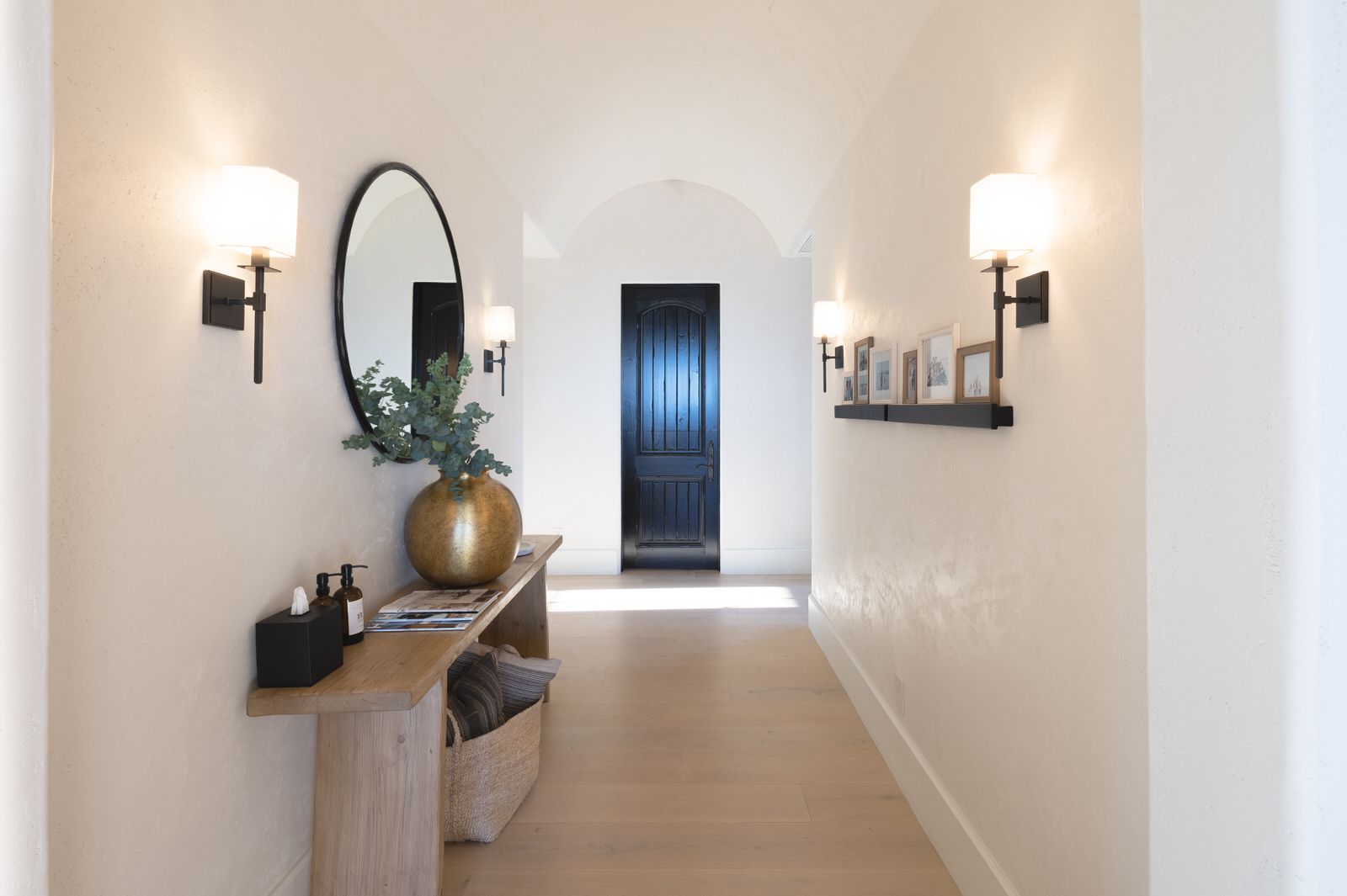 A long hallway with a table , mirror , and lamp.