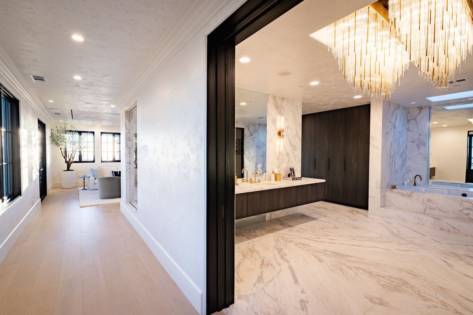 A hallway leading to a bathroom with a chandelier hanging from the ceiling.