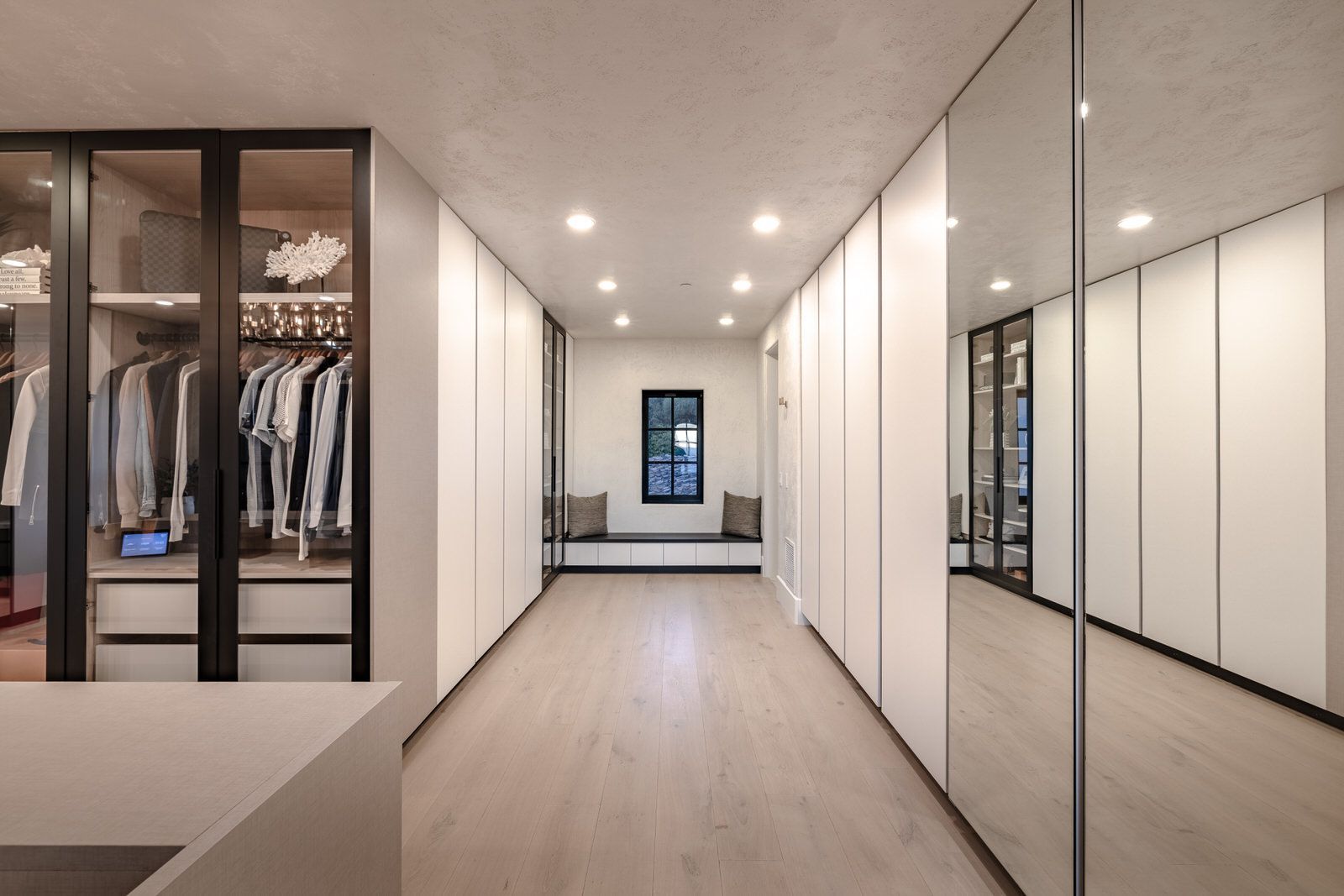 A walk in closet with lots of clothes and mirrors.