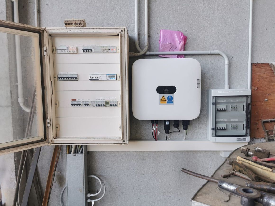Quadro elettrico con contatori e interruttori montati a parete, con attrezzi su un banco da lavoro in un locale di servizio.